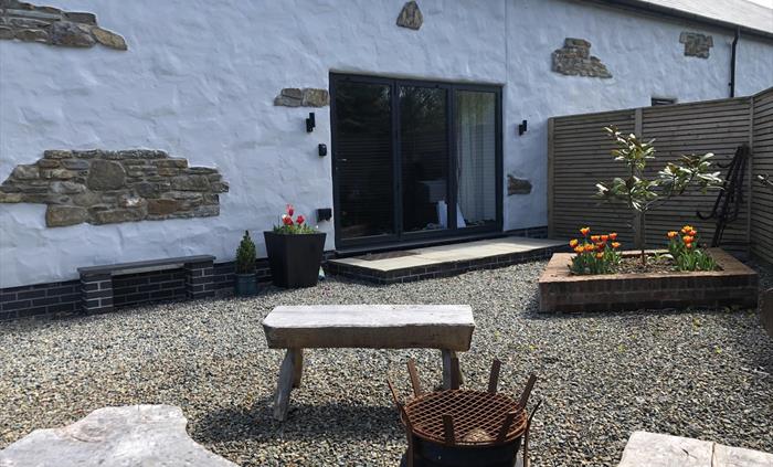 Fire bowl and seats on the front patio. Planter with Magnolia Tree and tulips. Entrance to the property via folding patio doors.